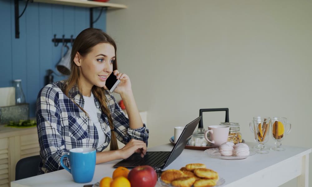 A person on the phone with a laptop at a kitchen counter at home
